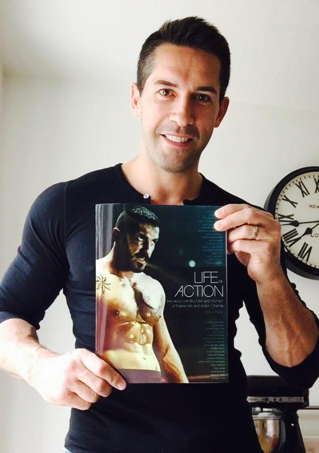Scott Adkins holding the book Life of Action by Mike Fury