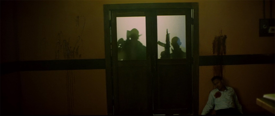 silhouette of two men waiting with big guns seen through double doors with frosted windows on the top half from Headshot movie