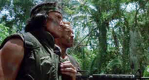 Predator movie Billy and Dutch stare into the jungle seeing nothing as Billy the Indian Tracker rubs his medicine pouch