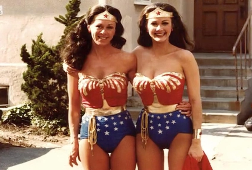 Jeannie Epper and Lynda Carter in matching Wonder Woman costumes stand hip to hip, smiling brightly, with an arm around each other